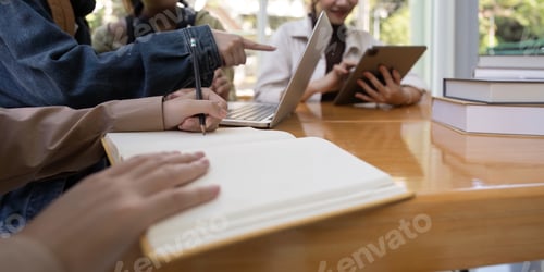 Preview: University students sitting together at table with book and laptop. Happy young people doing group