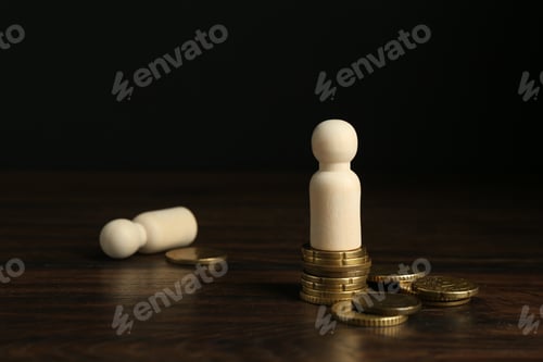 Preview: Financial inequality. Wooden figures with uneven amount of coins on table