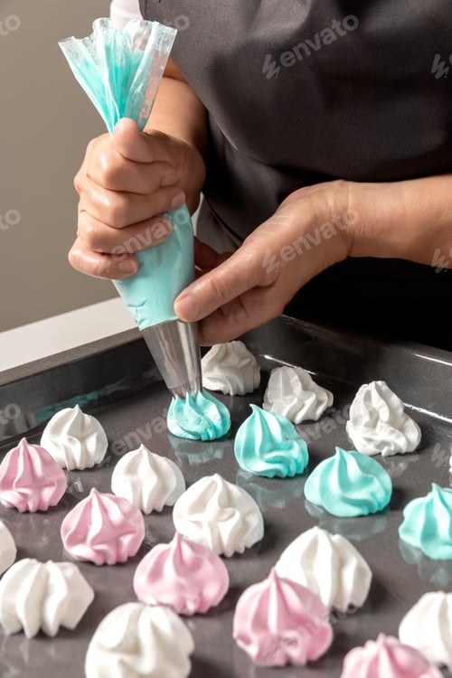 Preview: Woman hands squeeze colored meringue on a baking sheet to be baked