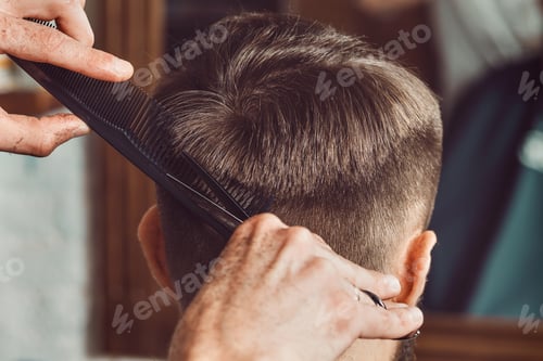 Preview: The hands of young barber making haircut to attractive man in barbershop