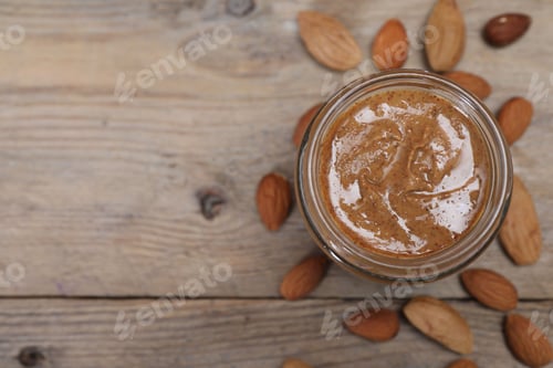 Preview: Tasty almond nut paste in jar on wooden table, top view. Space for text