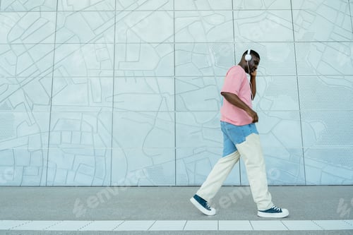 Preview: A man in a pink shirt and blue jeans is walking down a sidewalk while talking on his cell phone