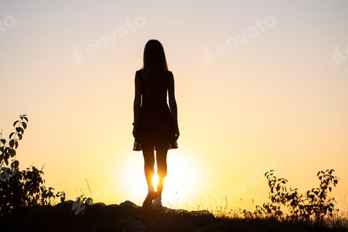 Vista previa: Dark silhouette of a young woman standing on a stone enjoying sunset view outdoors in summer