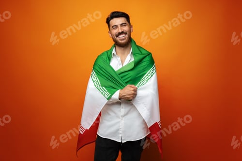 Preview: Portrait of a young casual man holding flag of Iran against orange background