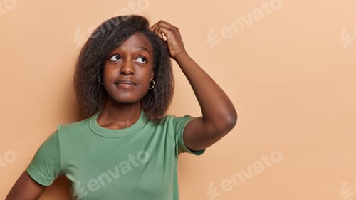Preview: Doubtful dark skinned woman scratches head with hesitation has confused unaware expression thinks