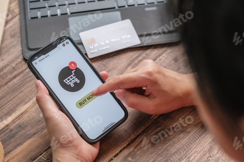 Preview: close up woman hand add product to card at shopping online mobile app on wood table at home