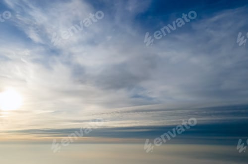 Preview: Aerial view of bright yellow sunset over white dense clouds with blue sky overhead.
