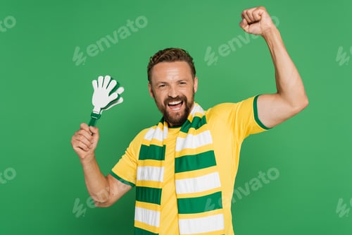 Preview: excited football fan in striped scarf holding plastic hand clapper isolated on green
