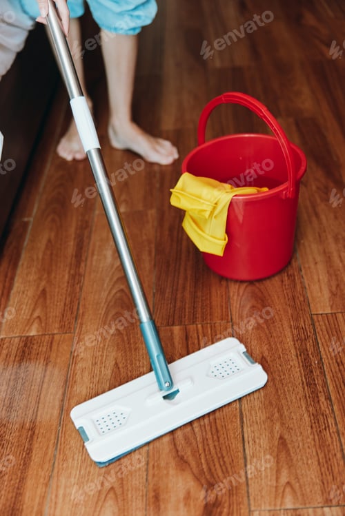 Preview: Woman cleaning wooden floor with mop and bucket of cleaning solution in front of red bucket and