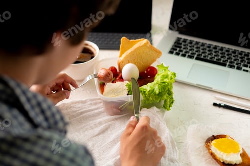 Preview: young male taking meal in front of the laptop while working, bad habit and obesity concepts