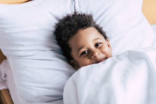 Preview: portrait of happy african american little boy lying under blanket in bed