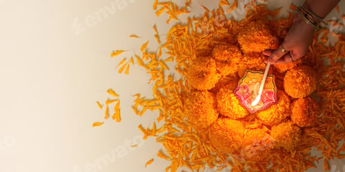 Preview: Diwali Festival. Hands lighting a decorative lamp surrounded by marigold flowers.
