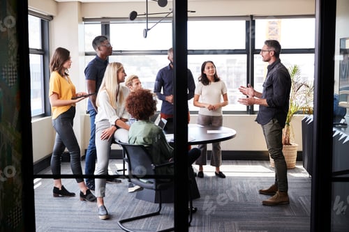 Preview: Creative business team in a meeting room listening to an informal presentation, seen from doorway