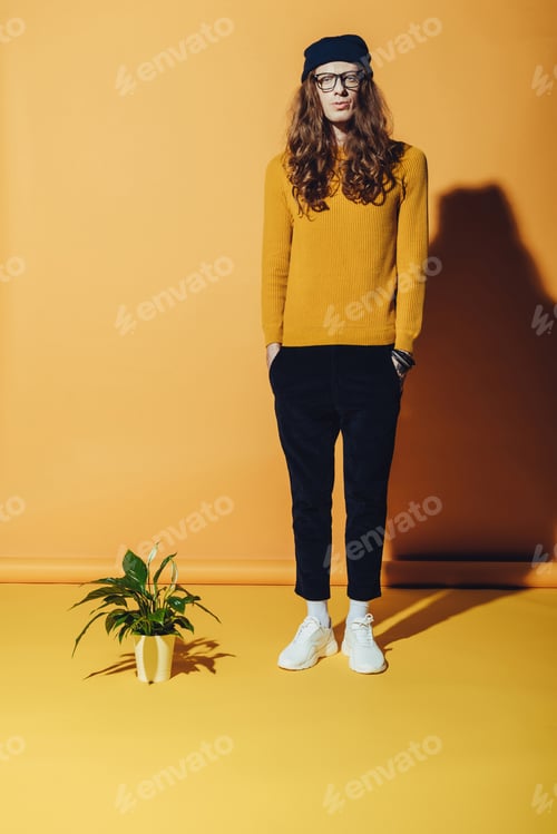 Preview: fashionable man with long hair standing near plant, on yellow
