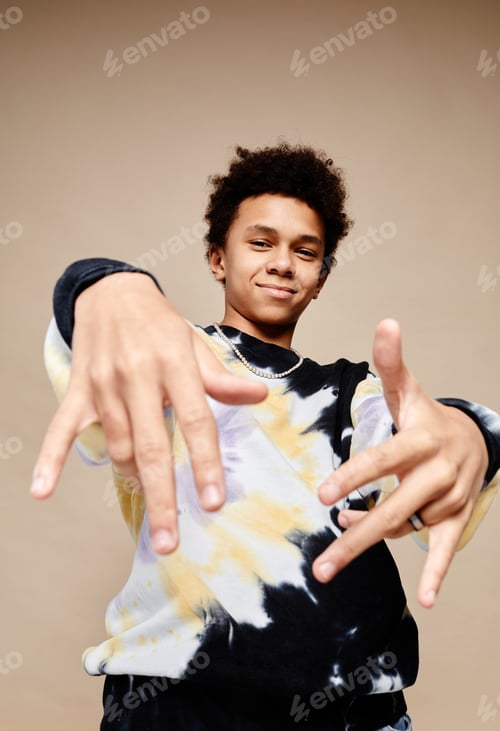 Preview: Vertical portrait of black teenage boy wearing tie dye shirt and smiling at beige background
