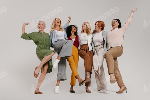 Preview: Multi-ethnic group of happy mature women embracing and dancing against grey background