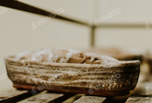 Preview: Baking bread. Dough in proofing basket on wooden table with flour, cumin and wheat ears. Top view.