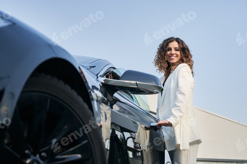 Preview: Young business lady standing near her black car.