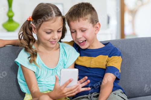 Preview: Happy boy sitting on sofa and using mobile phone in living room
