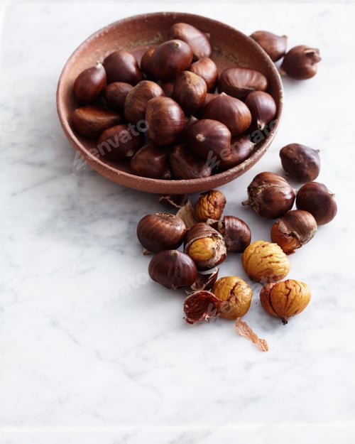 Preview: Chestnuts in and around a rustic bowl on a white surface.