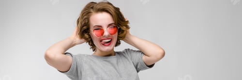 Preview: Charming young girl in a gray T-shirt on a gray background. Happy girl in red glasses