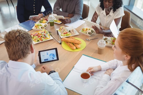 Preview: Businesswoman holding coffee cup while colleagues using digital tablets around breakfast table