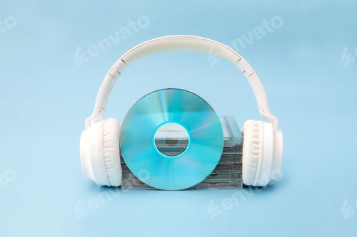 Preview: White wireless headphones holds a compact disc in front of a stack of jewel cases on blue background