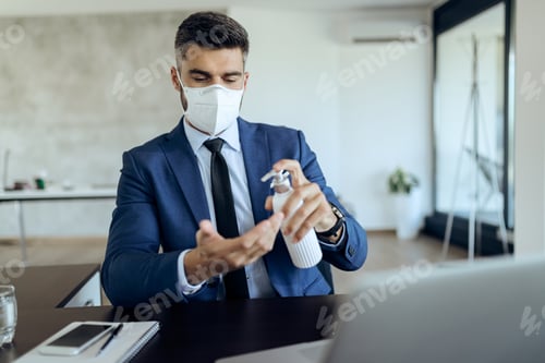 Preview: Entrepreneur with protective face mask using hands sanitizer in the office.