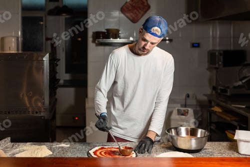 Preview: pizza man adds tomato to a pizza in a pizzeria restaurant kitchen