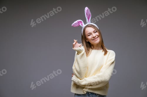 Preview: smiling young girl with bunny ears shows a mini heart with fingers