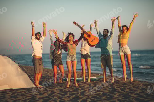 Preview: Happy friends sitting on the beach singing and playing guitar during the sunset