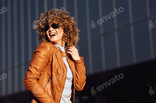Preview: Portrait of a young happy woman in a brown leather jacket with blond afro curly hair