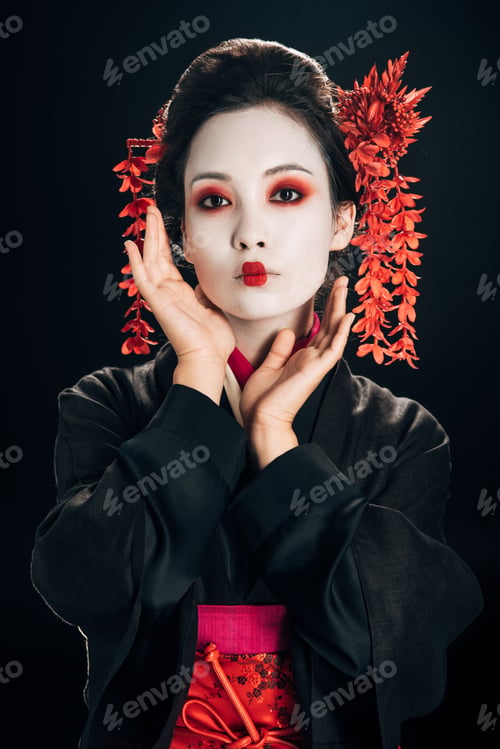 Preview: geisha in black and red kimono and flowers in hair with hand near face isolated on black