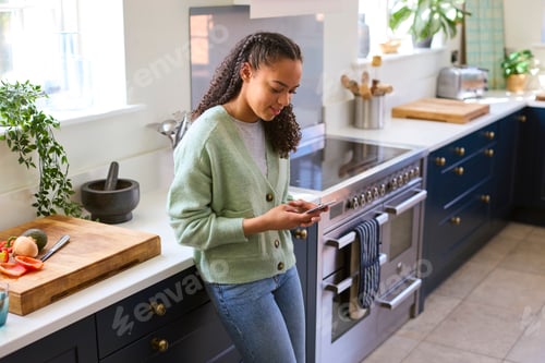 Preview: Teenage Girl At Home In Kitchen Connecting With Friends On Social Media Using Mobile Phone