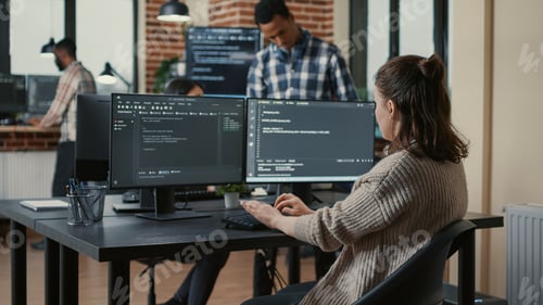 Preview: Focused software developer writing code looking at multiple computer screens