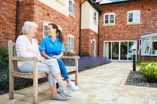 Preview: Senior Woman Sitting On Bench And Talking With Nurse In Retirement Home