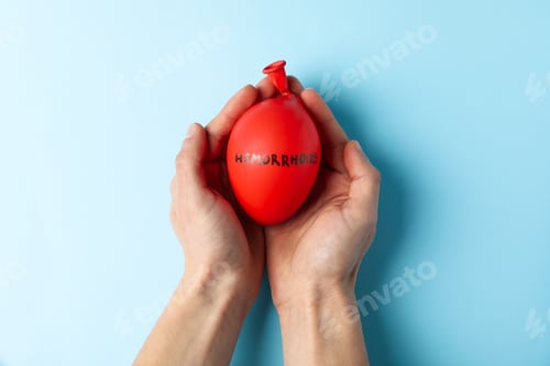 Preview: Hands hold balloon with inscription Hemorrhoids on blue background, top view