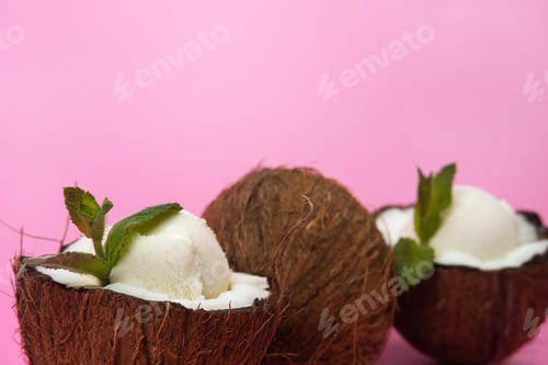 Preview: Vanilla ice cream balls in fresh coconut halves decorated with mint leaves on a pink background