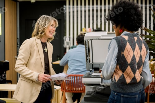 Preview: Women coworkers smiling while printing documents at office