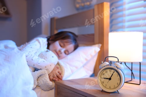 Preview: Little girl sleeping in bed at home, focus on alarm clock