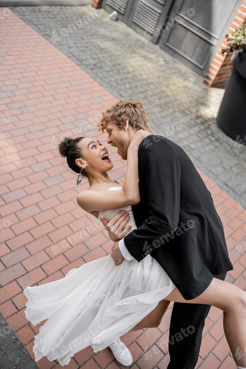 Preview: young elegant groom hugging excited african american bride, wedding in european city