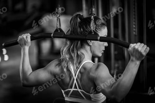 Preview: Female athlete exercising on a lat machine in a gym, black and white