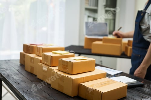 Preview: A man is working at his desk, preparing parcel boxes for shipment.He checks packs items carefully