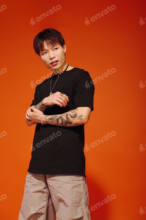 Preview: Stylish young man poses confidently against vibrant orange backdrop in urban setting