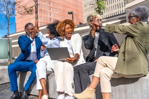 Preview: Excited business people celebrating news while using laptop outdoors