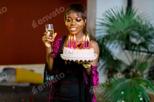 Preview: Beautiful African girl with birthday cake and with lighting candles and champagne