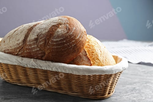 Preview: Loaves of tasty fresh bread in wicker basket on grey table, closeup