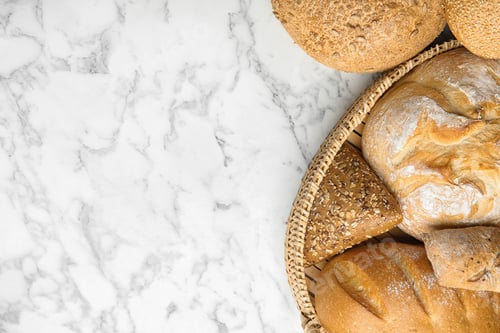 Preview: Loaves of different breads on white marble background, flat lay. Space for text