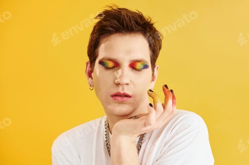 Preview: Young gay man is standing in the studio and posing for a camera. Rainbow make up
