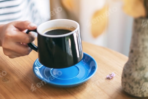 Preview: Closeup image of a woman's hand holding a black cup of hot coffee on wooden table